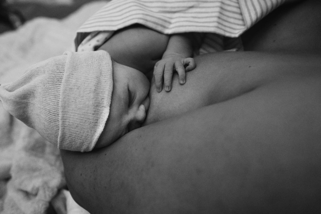 Brand new baby girl breastfeeding on bed at home during home birth in Kansas City 