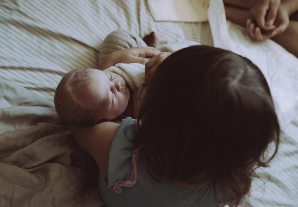 Big sister holding brand new baby sister after she was born at home