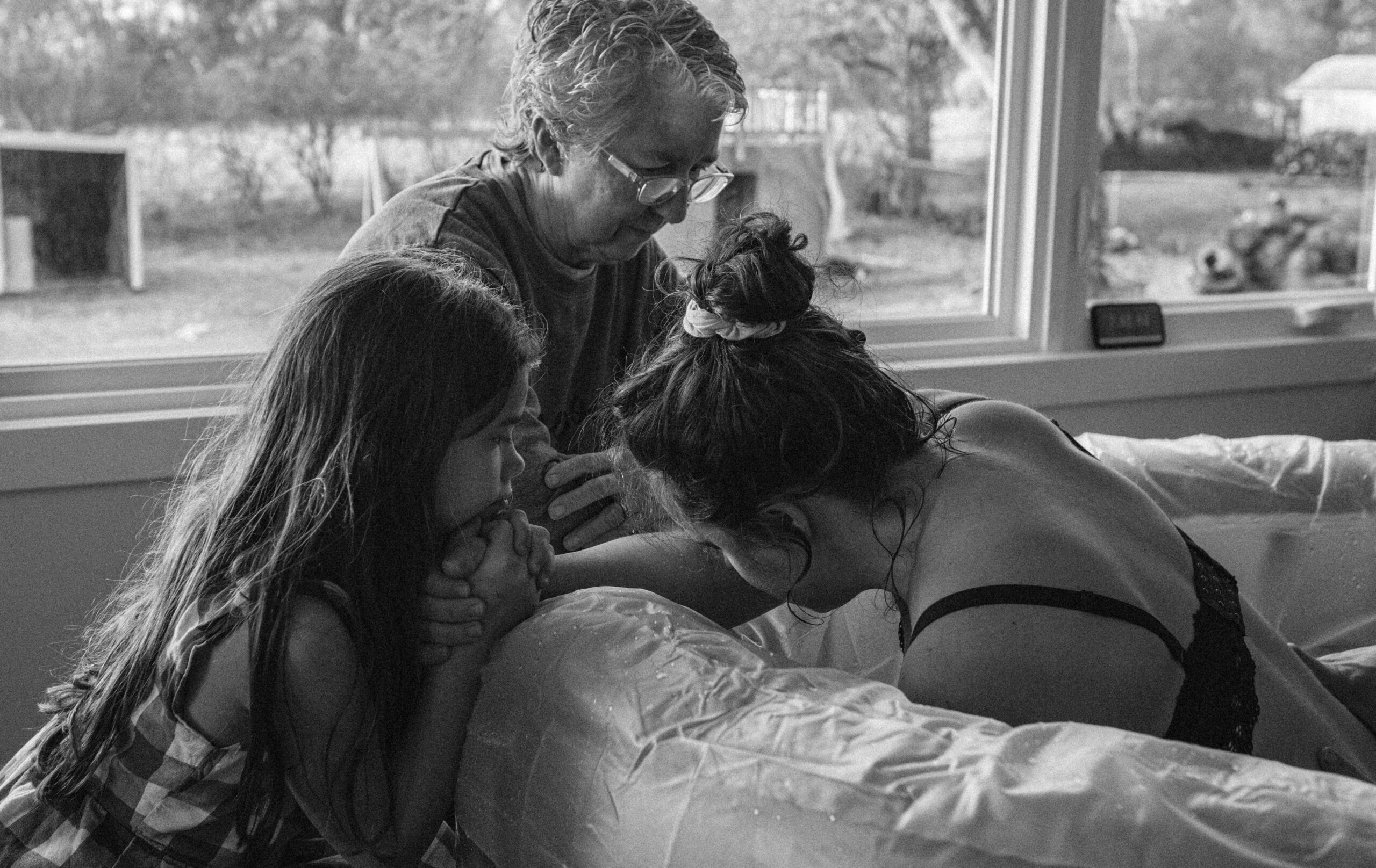 A mother in labor holds her older daughter's hand in her living room, capturing a raw and emotional moment of strength, love, and connection.